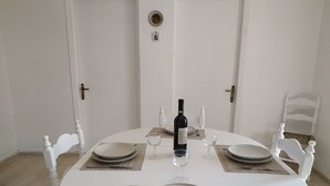 Ein runder Esstisch mit weißen Stühlen, eine Weinflasche und zwei Weingläser für zwei Personen.