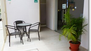 Un pequeño espacio al aire libre con una mesa y sillas, una planta en maceta y una puerta con un cartel que indica una habitación de hotel.