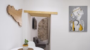 A modern interior with a round white table, a potted plant, a wooden wall art piece, a gray sofa, and a painting on the wall. - ARTEMIDE HOUSE - Superior Apartment Ortigia Wifi (Siracusa)