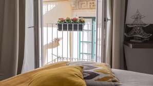 A bedroom with a bed, a window with curtains, a balcony with a railing, and a decorative item on the wall. - ARTEMIDE HOUSE - Superior Apartment Ortigia Wifi (Siracusa)