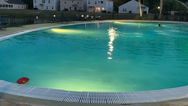 Piscina con indicatore di profondità di 1,5 metri, circondata da sdraio e un edificio sullo sfondo.
