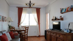 A living room with a sofa, dining table, chairs, a TV, and a wooden cabinet. - Cabo Roig 1 Bed Apt, Sea Views, Communal Pool, fun, Food and Entertainment (Orihuela Costa)