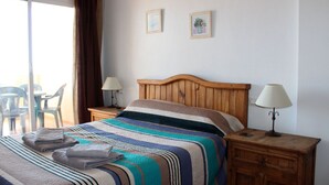A hotel room with a bed, two bedside tables, a window with curtains, and two wall-mounted pictures. - Cabo Roig 1 Bed Apt, Sea Views, Communal Pool, fun, Food and Entertainment (Orihuela Costa)