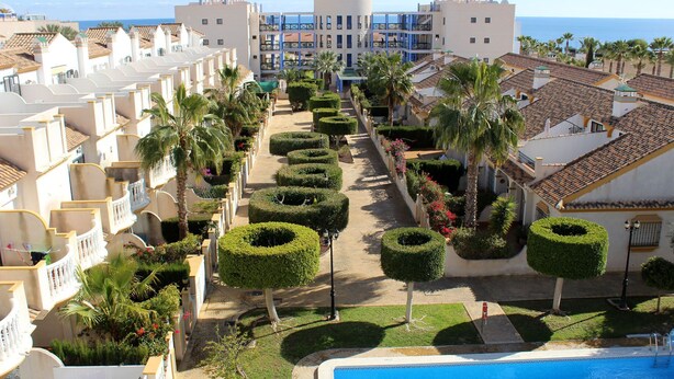 A resort with a pool, neatly trimmed hedges, and a view of the sea. - Cabo Roig 1 Bed Apt, Sea Views, Communal Pool, fun, Food and Entertainment (Orihuela Costa)