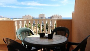 A balcony with a round table and chairs, overlooking a coastal area with buildings and a clear sky. - Cabo Roig 1 Bed Apt, Sea Views, Communal Pool, fun, Food and Entertainment (Orihuela Costa)