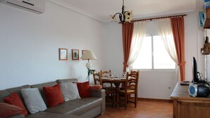 A living room with a sofa, dining table, chairs, a lamp, and a TV. - Cabo Roig 1 Bed Apt, Sea Views, Communal Pool, fun, Food and Entertainment (Orihuela Costa)