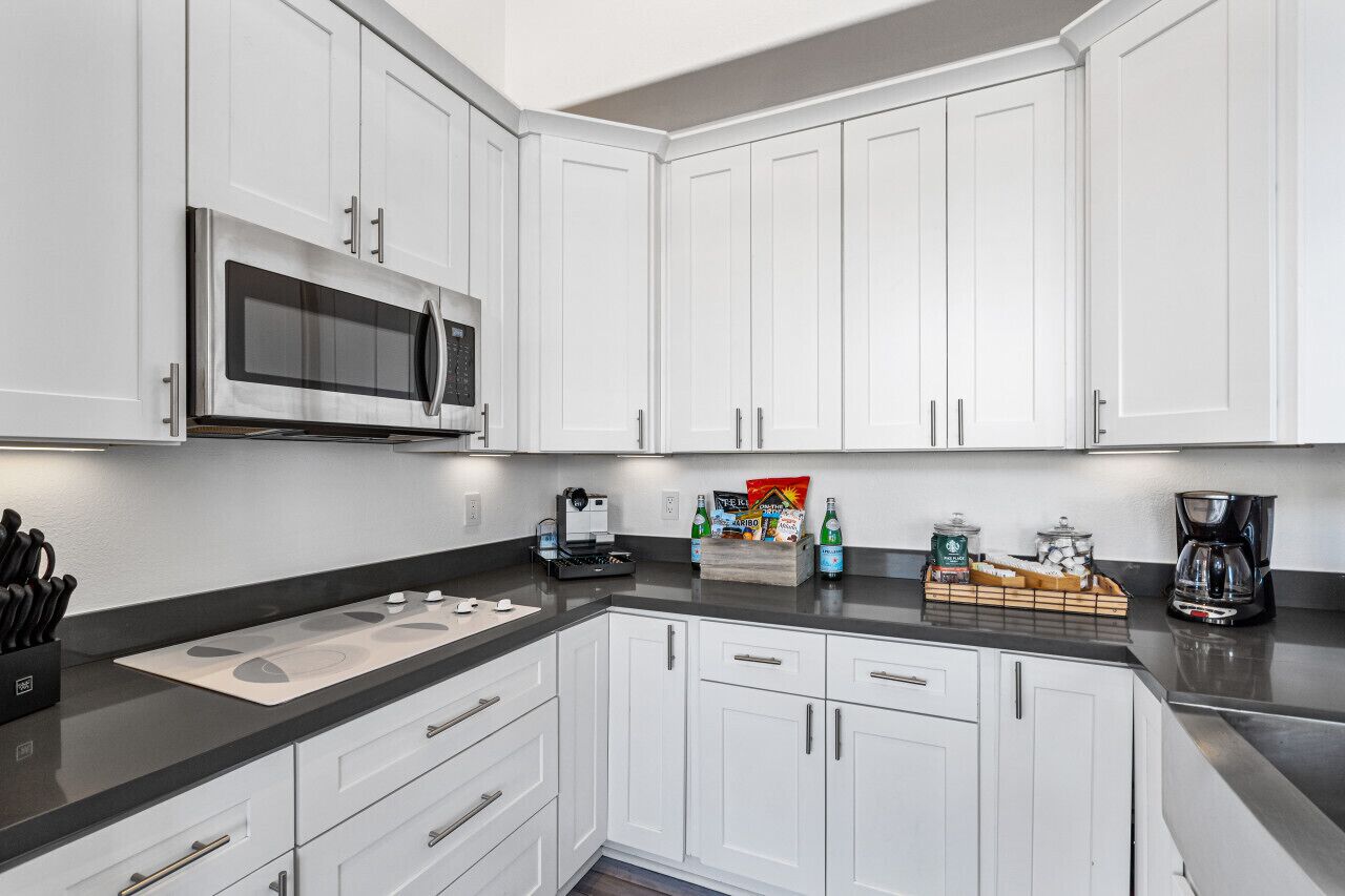 A modern kitchen with white cabinets, a stainless steel microwave, a coffee maker, and a box of bottled water.
