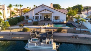 Ein Haus mit Pool, ein vor Anker liegendes Boot und eine Terrasse mit Gartenmöbeln.