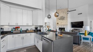 Eine moderne Küche mit weißen Schränken, einer zentralen Kochinsel und einem Essbereich mit Sofa und Fernseher.