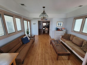 A spacious living room with hardwood flooring, a brown sofa, a glass coffee table, and a white cabinet.
