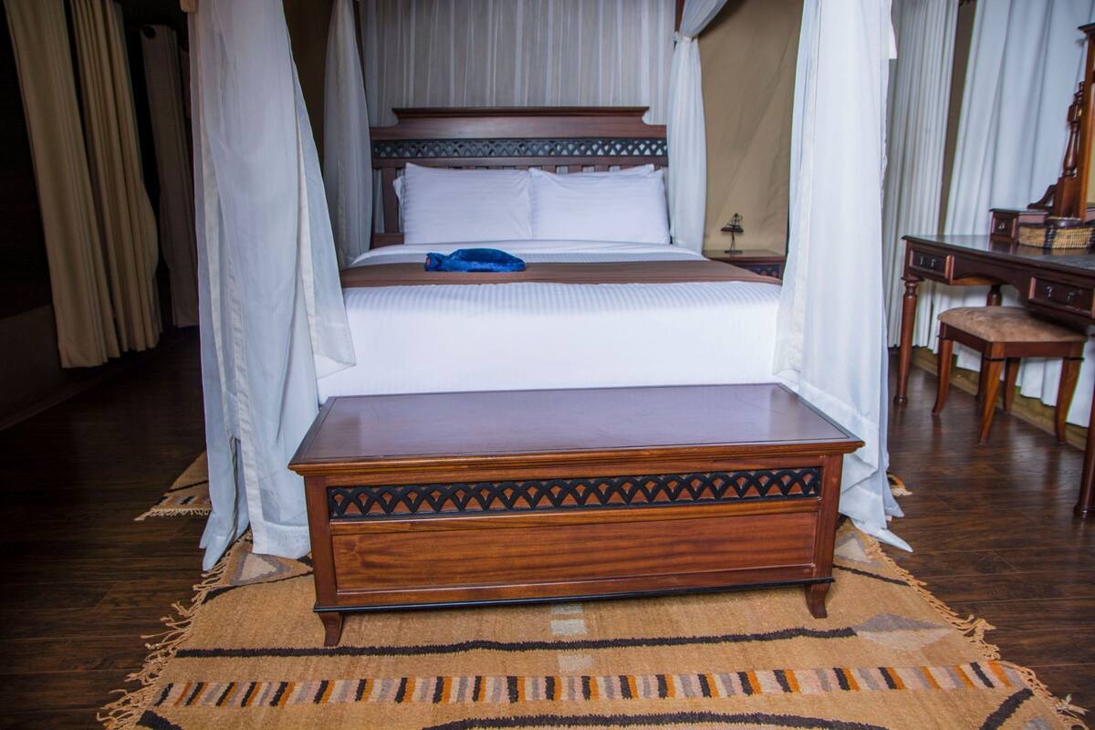 A four-poster canopy bed with white linens, a wooden bedside table, and a patterned rug.