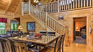A wooden cabin interior with a dining area, a staircase, and a bedroom.