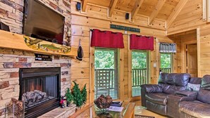A cozy log cabin interior with a stone fireplace, leather sofa, and a sign that reads "Live Well-Laugh Often-Love Much."