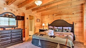 A wooden cabin bedroom with a bed, dresser, and a television on a dresser.