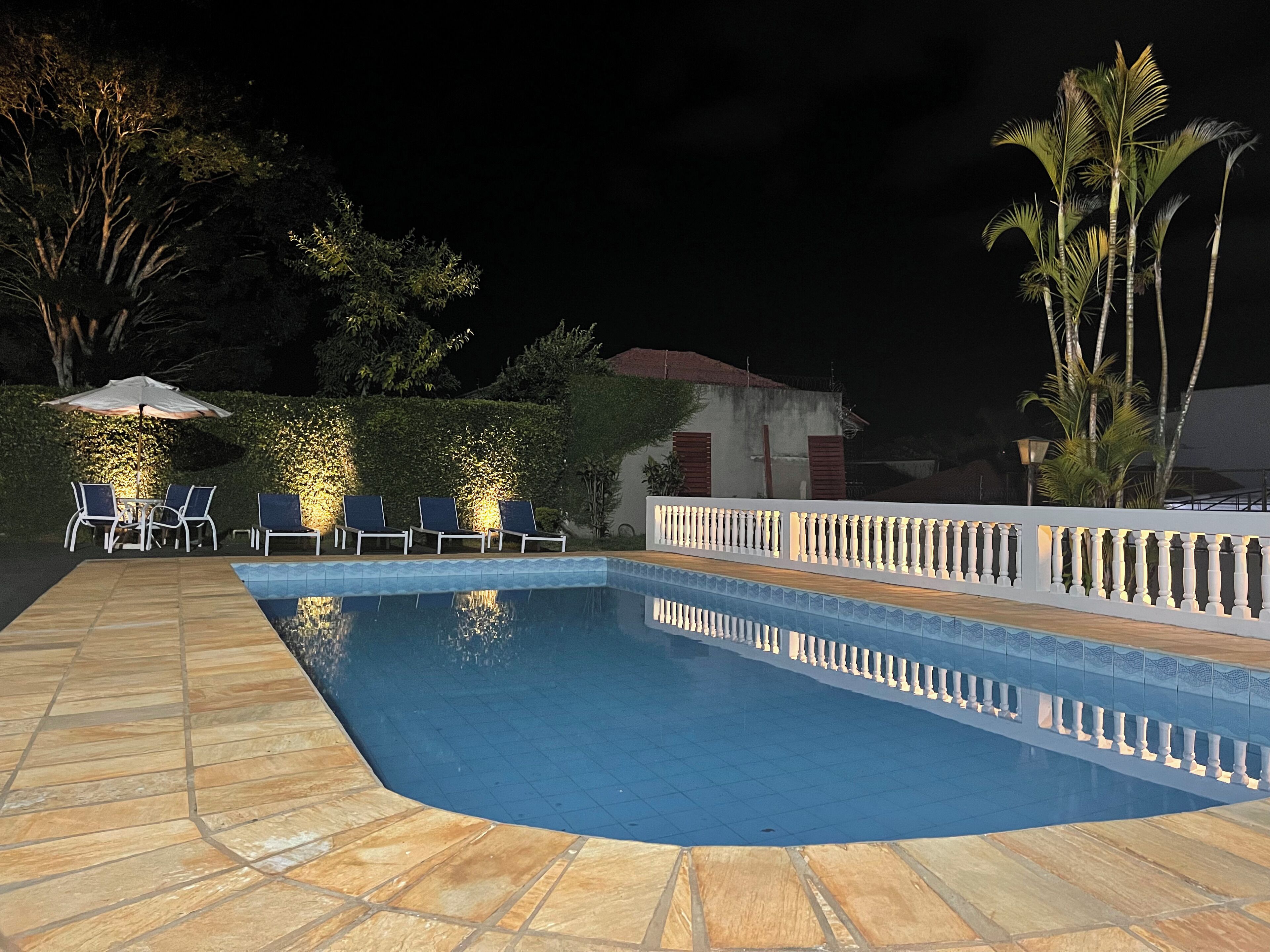 A swimming pool with a tiled deck, lounge chairs, and an umbrella.