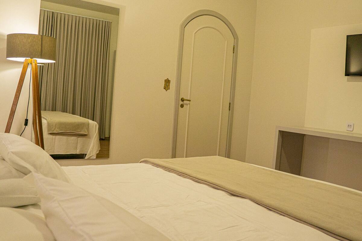 Una habitación de hotel con cama, mesita de noche, lámpara, televisor y puerta.