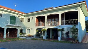 A two-story building with a tiled roof, multiple balconies with wrought iron railings, and a central courtyard with potted plants. - Dom Ravello (Telemaco Borba)