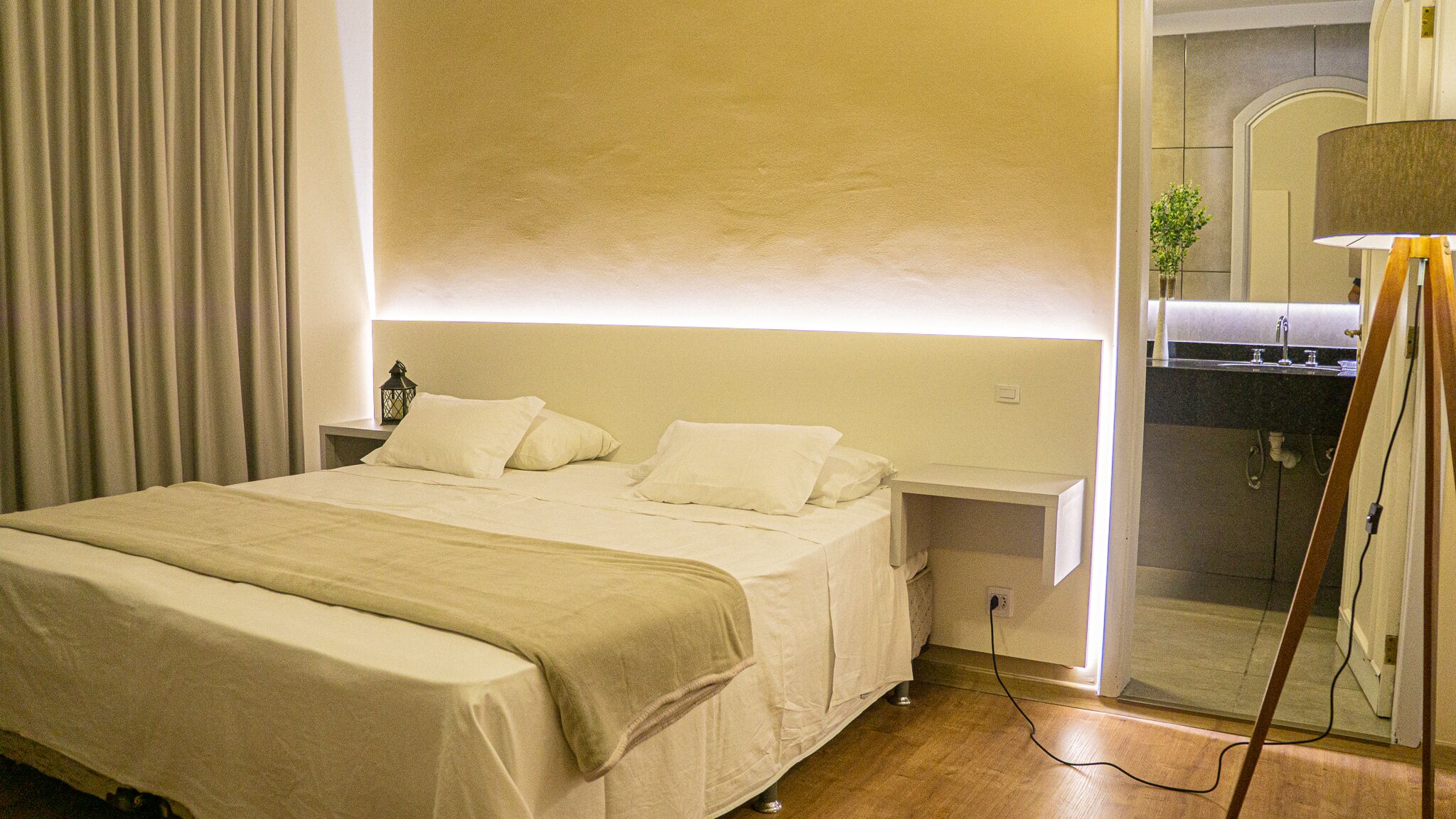 A hotel room with a bed, a nightstand, a lamp, and a bathroom visible through an open door.