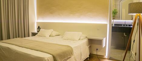 A hotel room with a bed, a nightstand, a lamp, and a bathroom visible through an open door.