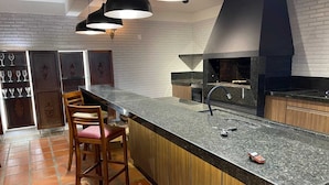 A modern kitchen with a granite countertop, wooden chairs, a black faucet, and a brick wall backsplash. - Dom Ravello (Telemaco Borba)