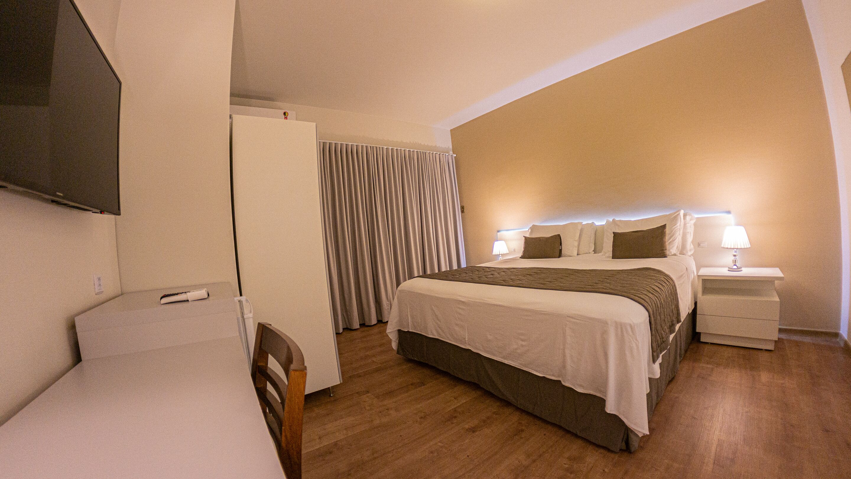 A hotel room with a bed, bedside tables, a TV, and curtains.