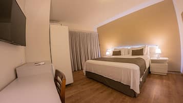 A hotel room with a bed, bedside tables, a TV, and curtains.