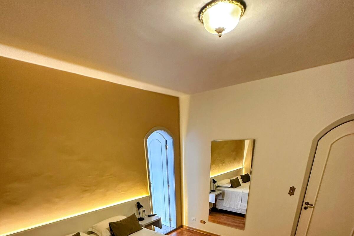 Una habitación de hotel con una cama grande, mesitas de noche, un espejo y una puerta.