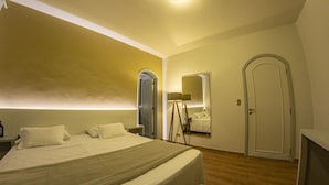 A bedroom with a large bed, a bedside table, a mirror, and a door. - Dom Ravello (Telemaco Borba)