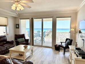 A spacious living room with a view of the beach, a ceiling fan, and a glass coffee table.