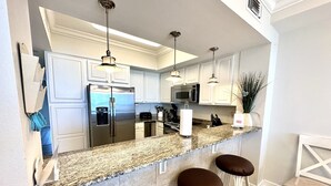 A modern kitchen with white cabinets, stainless steel appliances, granite countertops, and bar stools. - Sea Shell 3 Bedroom Townhouse by RedAwning (Navarre)