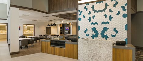 A modern hotel lobby with a reception desk, seating area, and a television screen.