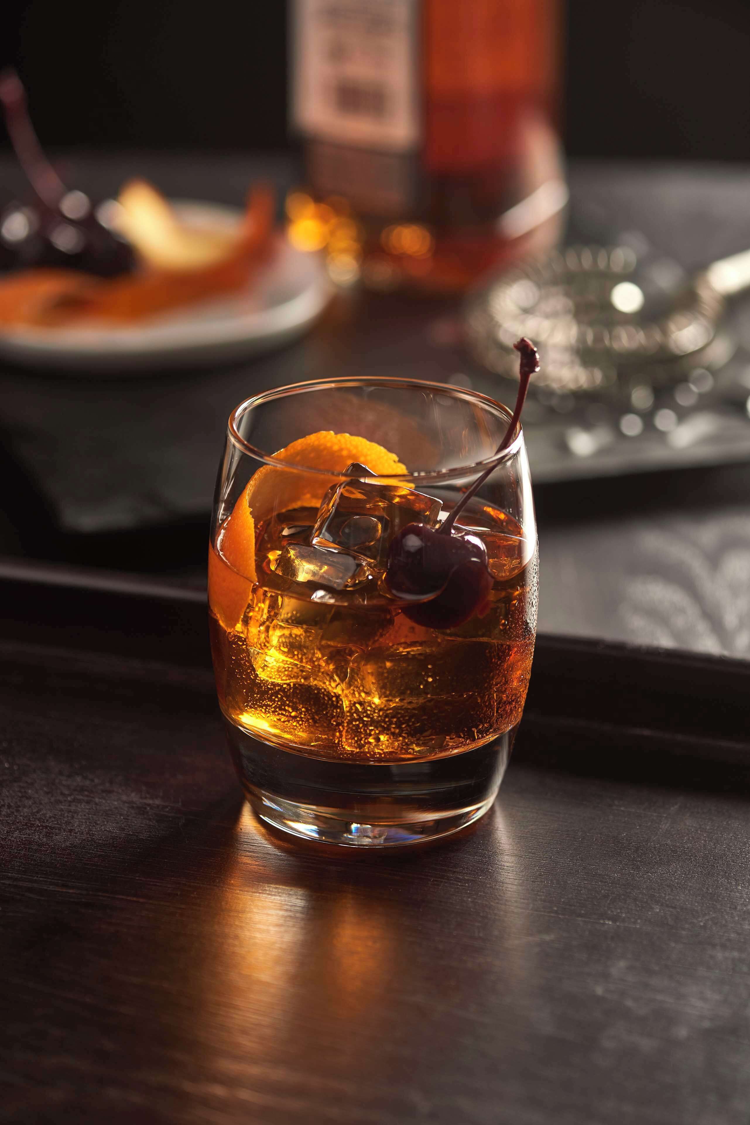 Un verre de whisky avec des glaçons et une cerise, posé sur une table en bois foncé.