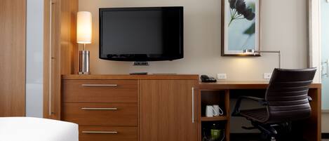 Een hotelkamer met een houten bureau, een flatscreen televisie, een lamp, een stoel en een lijstje aan de muur.