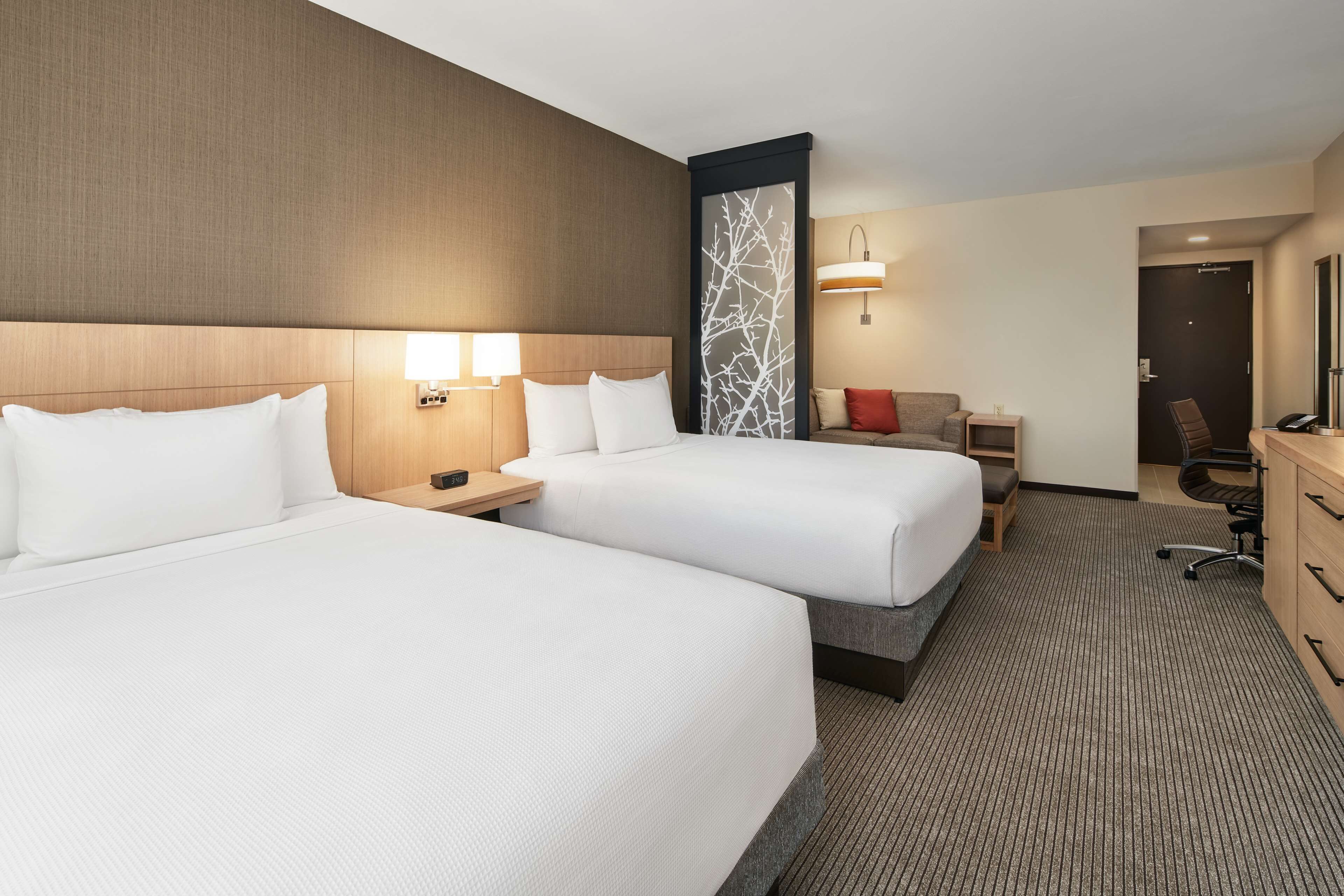 A hotel room with two beds, a desk, a chair, and a TV.