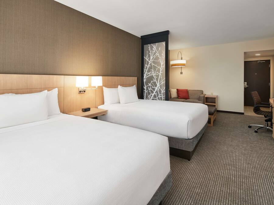 A hotel room with two beds, a desk, a chair, and a TV.