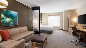 Habitación de hotel con sofá, una mesita, escritorio, silla, cama y televisor.