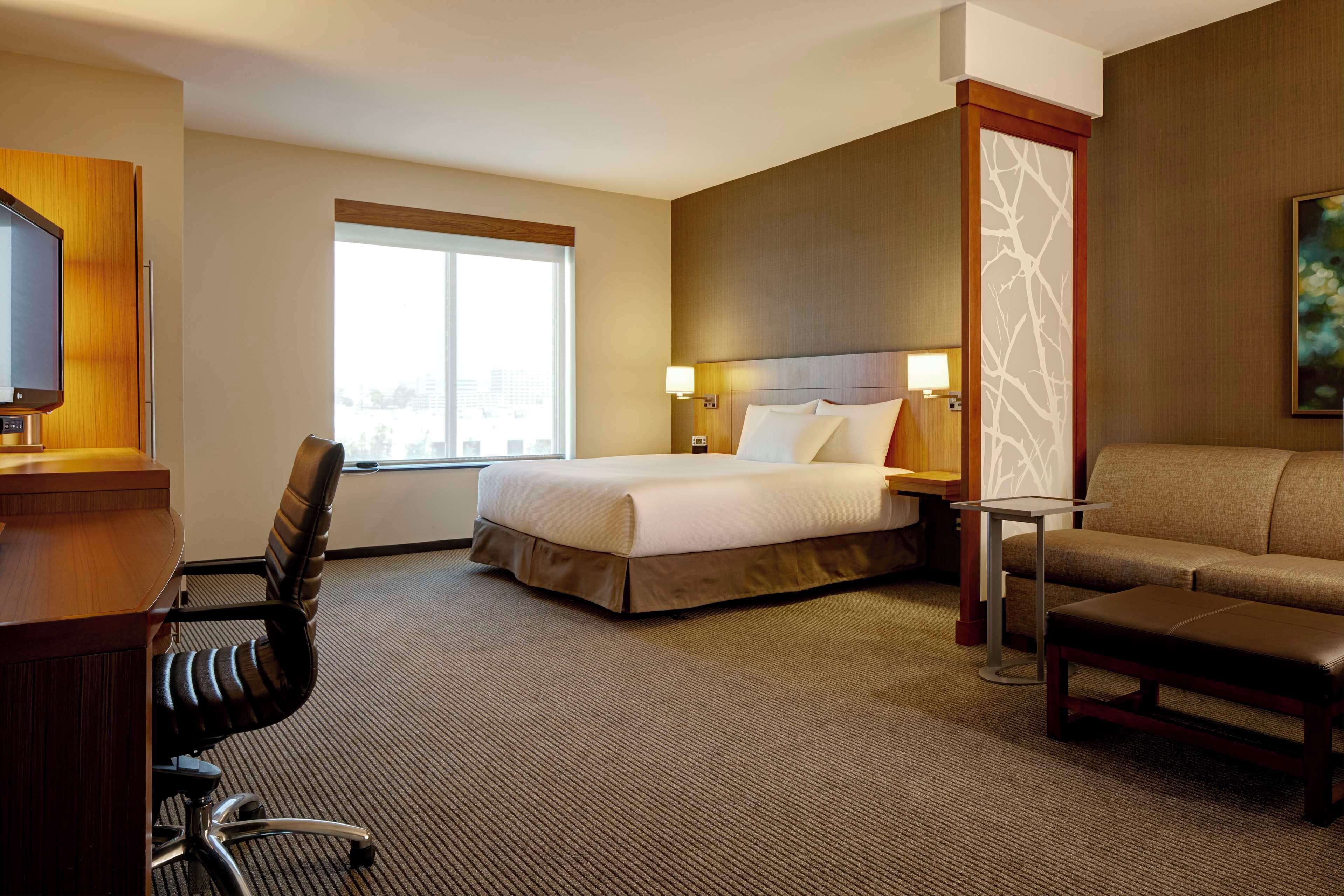 Una habitación de hotel con cama, escritorio, silla, sofá y ventana.