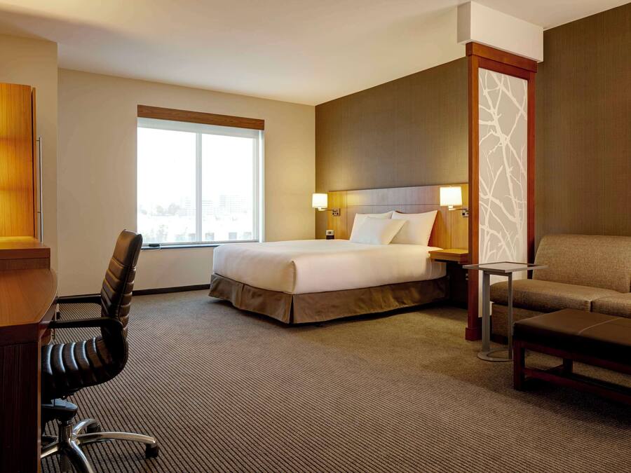 Una habitación de hotel con cama, escritorio, silla, sofá y ventana.