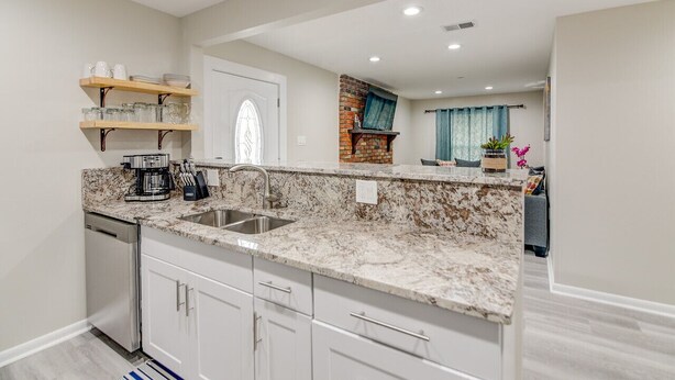A kitchen with white cabinets, a granite countertop, a built-in brick oven, and a window with a decorative design.