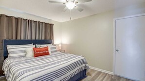 A bedroom with a bed, a ceiling fan, a nightstand, and a door.