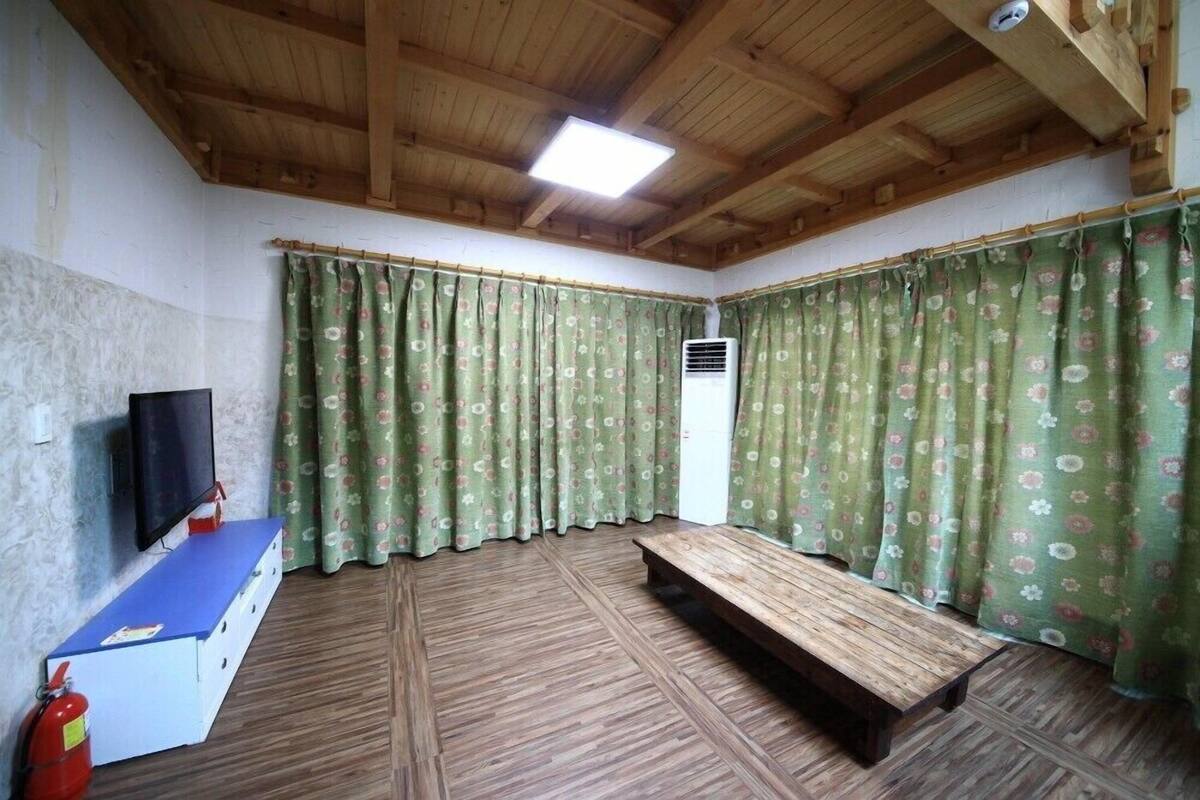 Ein Zimmer mit Holzboden, einem Flachbildfernseher, einer Bank und blumigen Vorhängen.