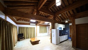Une pièce spacieuse avec des poutres apparentes, un plancher en bois, un coin cuisine équipé d’un réfrigérateur et un téléviseur.