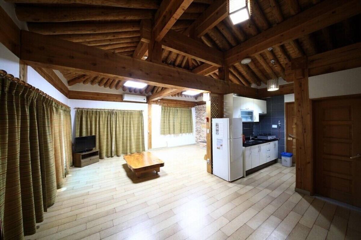 Ein geräumiger Raum mit Holzbalken, Holzboden, Küchenzeile mit Kühlschrank und Fernseher.