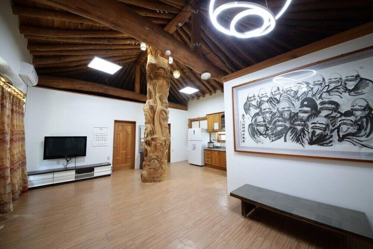 Ein geräumiger Raum mit Holzboden, einer großen Holzskulptur, einem Fernseher und einem gerahmten Kunstwerk an der Wand.