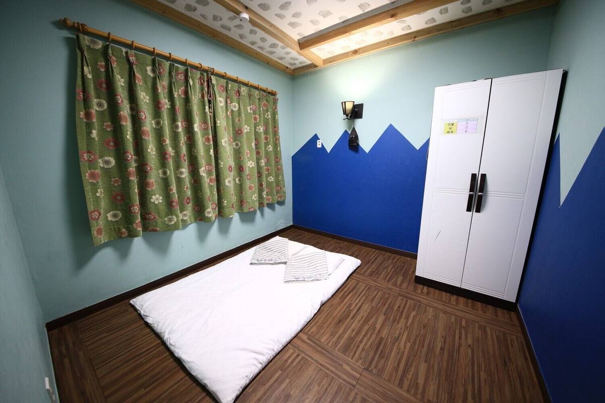 Ein Zimmer mit einem Bett, einem Kleiderschrank, einem Vorhang und einer Wand mit Bergmotiv.
