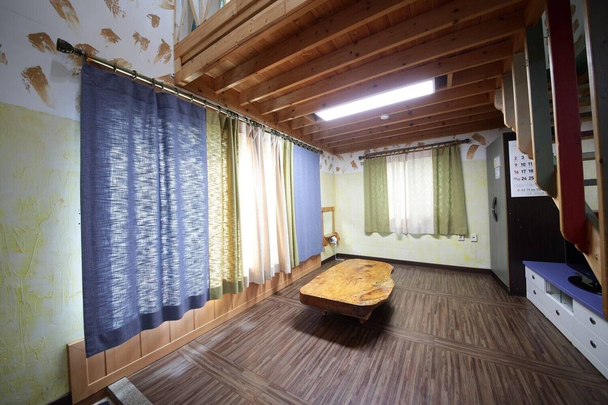 Ein Zimmer mit Holzboden, einer Holzbank und Vorhängen an den Fenstern.