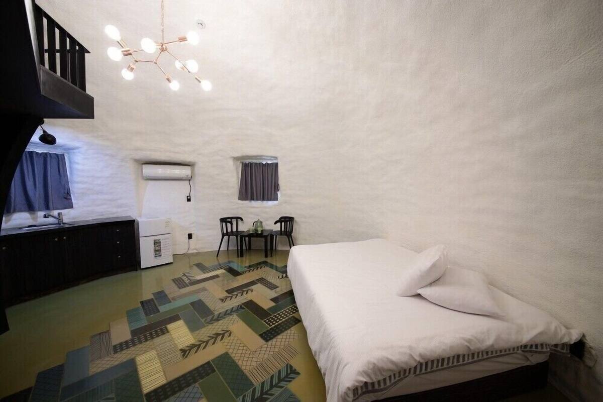 Ein Schlafzimmer mit einem Bett, einem Schreibtisch, einem Stuhl, einem kleinen Tisch und einer Pendelleuchte.