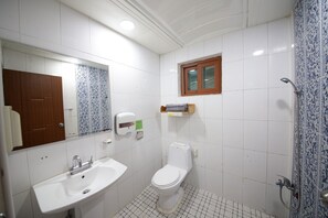 Een badkamer met een witte wastafel, toilet, douche, spiegel en een klein raam.
