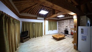 Un intérieur rustique avec un plafond en bois, une cheminée en briques, un téléviseur et des rideaux.
