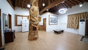 Une pièce spacieuse avec un plafond en bois, une sculpture en bois placée au centre, un réfrigérateur blanc, une table à manger et un climatiseur fixé au mur.
